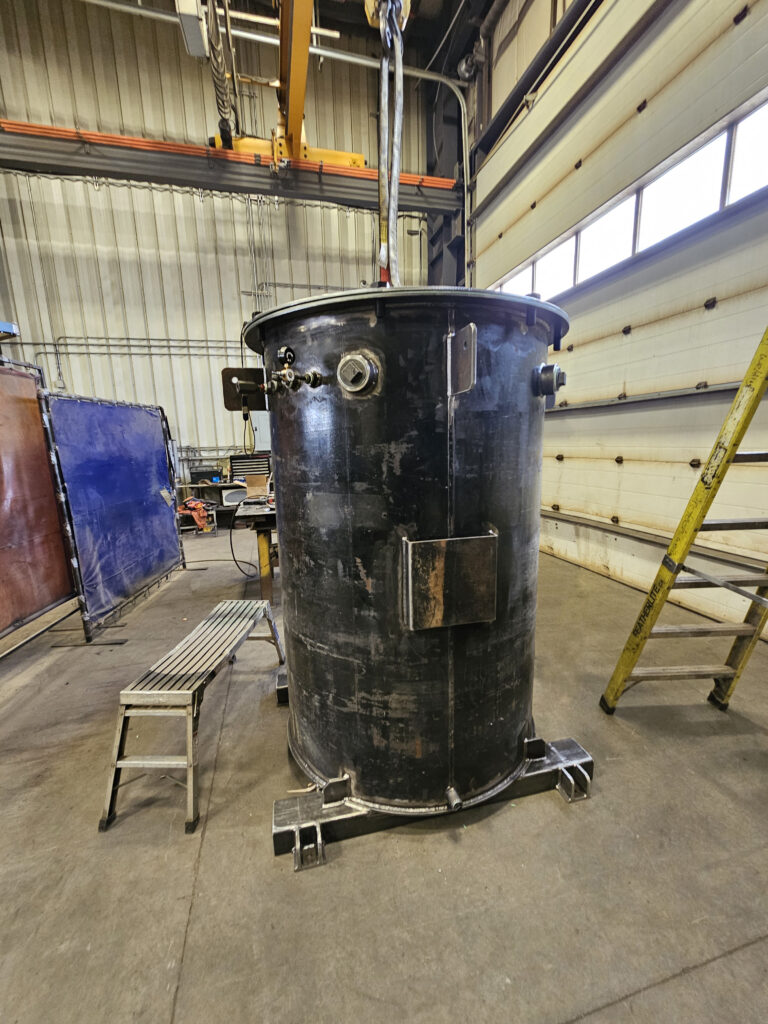 An industrial API 650 tank, constructed according to industry standards for storing oil, gas, chemicals, and other liquids. The cylindrical tank is equipped with a domed or conical roof, and features safety measures such as a ladder and railing for maintenance access. The tank is located in an open industrial setting and is surrounded by safety barriers.